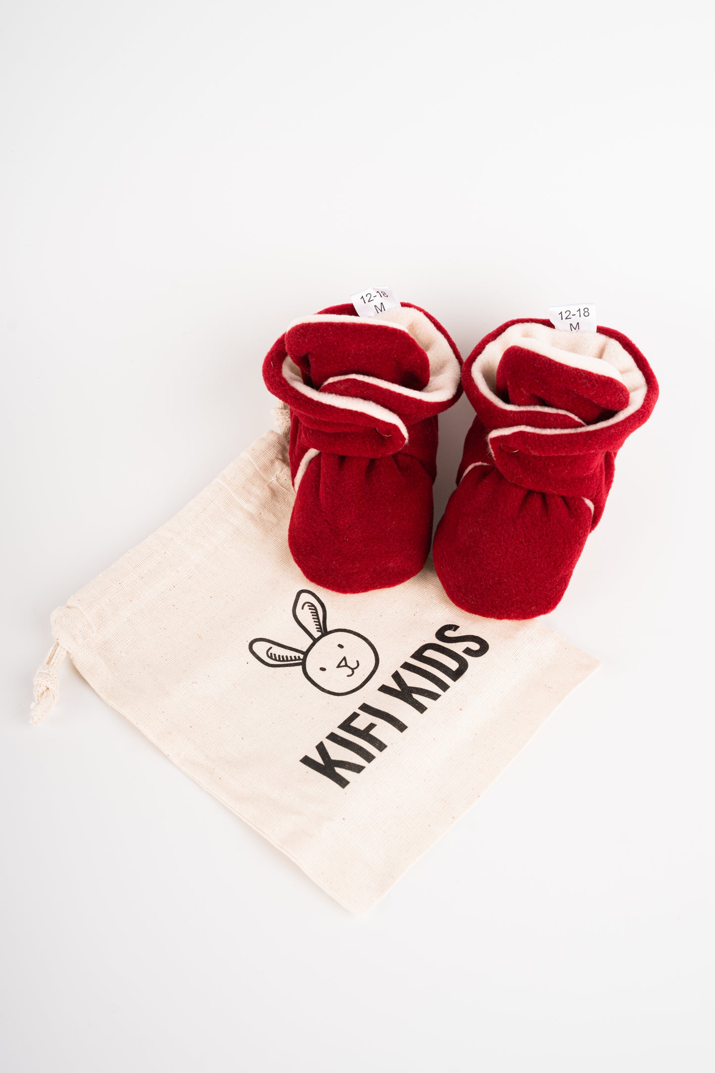 Comfortable and breathable baby booties in burgundy color with non-slip soles for safe adventures. View of pair of booties with bag.